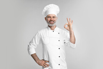 Wall Mural - Happy chef in uniform showing OK gesture on grey background