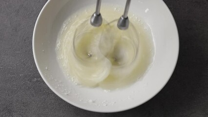 Sticker - Chef whips raw egg whites with powdered sugar in a white bowl with a mixer, top view. Close-up of food