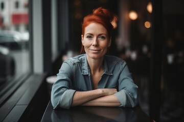 A woman with red hair is sitting at a table with her arms crossed