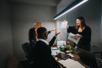 In a well-lit modern office, a multicultural team of coworkers is enthusiastically discussing various growth and sales statistics. The environment reflects a dynamic and collaborative workspace.