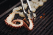 the cook turns over the tentacles of an octopus on the grill