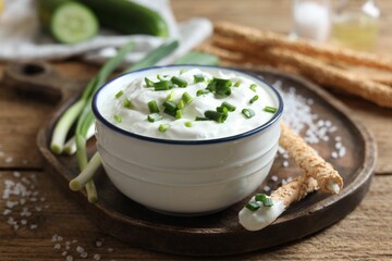 Delicious yogurt, green onion, grissini and salt on wooden table, closeup