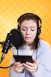 Narrator frowning while reading aloud from ebook on ereader into professional mi against backdrop, doing dramatic acting. Woman recording audiobook, reading text from tablet, portraying characters