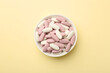 Different vitamin pills in bowl on pale yellow background, top view