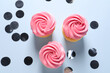 Delicious cupcakes with bright cream and confetti on light background, flat lay
