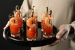 Woman holding tasty canapes with shrimps, tomatoes and sauce in shot glasses on black background, closeup