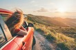 Happy woman enjoying the breeze with her head out of the car window while traveling through a beautiful landscape during a scenic sunset drive