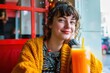 Happy young student sits cozily in a vibrant cafe, enjoying a fresh glass of orange juice, exuding warmth and contentment in a casual, urban setting