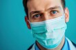 Close-up portrait of a male doctor wearing a surgical mask, with a focused expression, representing healthcare safety in challenging times against a turquoise backdrop
