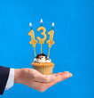 Hand delivering birthday cupcake - Candle number 131 on blue background