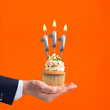The hand that delivers cupcake with the number 111 candle - Birthday on orange background