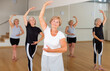 Portrait of interested senior lady learning classic dance moves during group class in studio.