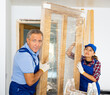 Male and female carpenters in uniform helping each other for installing wooden door indoors