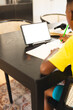 African American boy in yellow shirt writing in notebook using tablet, copy space