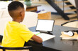 An African American boy in yellow shirt, studying at table using tablet, copy space