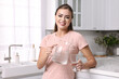 Happy woman with jug and glass of water in kitchen