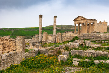 Wall Mural - View of weathered remains of Capitol Temple in Dougga, historic Roman archaeological site in Tunisia, with iconic columns and pediment, under clouded spring sky..