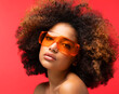 Young Afro woman wearing orange sunglasses smiling, isolated on studio red background.