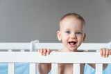 Fototapeta Miasto - A baby laughing out loud reaches out from his crib with his hand