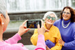 Three elderly friends in bright sweaters take a photo on a smartphone and laugh, having a great time.