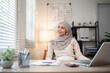 © wichayada - Muslim businesswoman working using laptop and taking notes on documents In the modern office