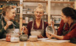 A company of three young women friends are painting ceramics in a pottery workshop.