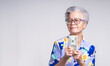 Senior Asian woman with money in her hands and looking at the camera, isolated on a gray background.