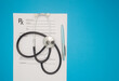 Top view of a stethoscope over the medical prescription sheet on a blue background.