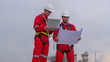 Engineer wear uniform and helmet stand workplace hand holding tablet computer, survey inspection team work see detail blue print plant site to work with oil refinery  background.
