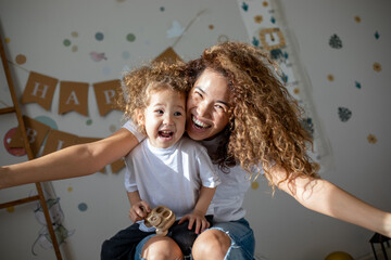 Curly mother and child play against the background of the inscription 