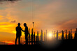 Silhouette of Engineer and worker team checking project at building site background, a construction site with sunset