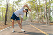 © kudosstudio - Young female runner stretching her arms and legs before starting her morning run at a local running park