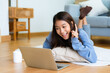Young asian woman smile working in living room at home. Happy female using computer laptop and lying on the floor at house, Video call with friend