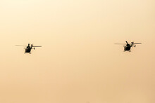 Two Silhouette Helicopters Are Flying On Isolated Dawn Sky