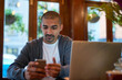 © peopleimages.com - Laptop, cellphone and businessman in cafe working on creative web design for startup company. Technology, freelancer and male copywriting editor with computer and phone for online research project.