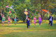 Happy Asian Thai group of boys and girls wear traditional colorful farmer outfits and run with flying kites on a green field.