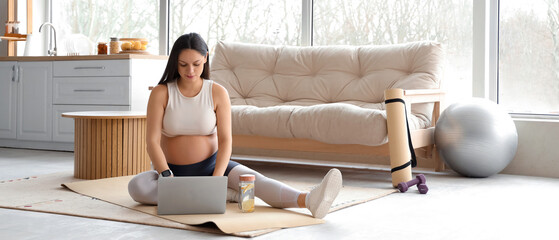 Canvas Print - Sporty pregnant woman using laptop on mat at home