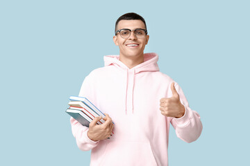 Poster - Handsome young man with books showing thumb-up on blue background