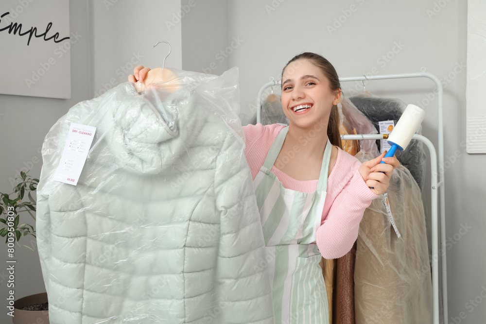Young female worker with lint roller and puffer jacket at dry-cleaner's