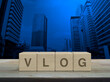 Vlog letter on wood block cubes on wooden table over modern office city tower and skyscraper, Vlog video marketing concept