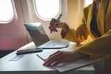 Fototapeta  - Attractive Asian businesswoman passenger sits on a business class luxury plane while taking notes on business, working with a tablet during a flight on an international trip.