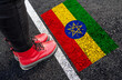 a woman with a boots standing on asphalt next to flag of Ethiopia and border
