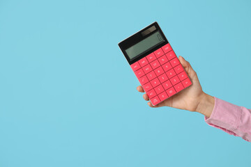 Wall Mural - Female hand with calculator on blue background