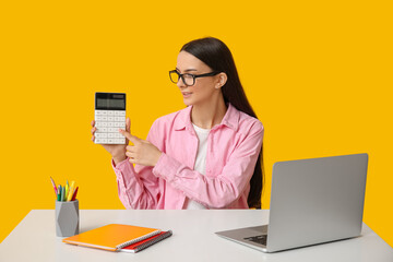 Wall Mural - Beautiful young woman with calculator, modern laptop and notebooks at table on yellow background