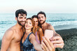 Group of joyful friends capture a selfie with the ocean backdrop - happiness and togetherness on a sunny beach day.