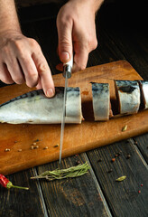 Wall Mural - A man hands cut mackerel on a kitchen board before frying. The concept of preparing a fish dish for dinner.