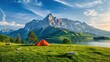 © Hryhor Denys - A bright orange tent pitched on a grassy field next to a lake in a beautiful mountain landscape