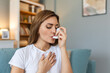 Woman using inhaler while suffering from asthma at home. Young woman using asthma inhaler. Close-up of a young woman using asthma inhaler at home.