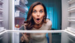 © Alberto Masnovo - Extreme close-up of a young shocked woman looking in empty fridge at home, view from inside the refrigerator. Generative Ai.