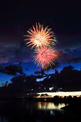 Sticker - fireworks lighting up the sky over water at night, with buildings in the background